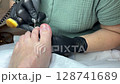 Professional pedicure session. Toenail care treatment. Woman foot cleaning. Nail technician working. Beauty salon procedure. Foot hygiene service. Spa therapy moment. Black gloves and machine. 128741689