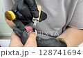 A manicure master in black gloves and a protective mask gives a manicure to a girl. Close-up of a cosmetologist's hand filing a woman's nails in a beauty salon. The concept of health and beauty 128741694
