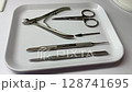 Closeup of clean professional manicure instruments on a white tray. Includes metal cuticle pushers, nippers, scissors, and drill bits. High-key background, suitable for nail salon advertisements 128741695
