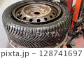 Close-up of a used car tire with visible tread and rusty steel rim being mounted on a tire machine. Scene from a garage workshop during seasonal tire change or maintenance. Technical auto content. 128741697