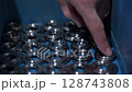 Close-up of a worker's finger arranging precision-machined metal components in a blue bin under controlled lighting. Concept of organization, order, and manufacturing workflow 128743808
