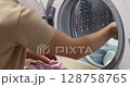 female hand loading colour laundry into the drum of a home washing machine. 128758765
