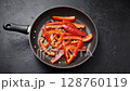 Sauteing red bell peppers in pan over black background culinary cooking progression 128760119