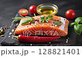 A large piece of salmon fillet, with its skin and bones removed, is placed on a black surface. The salmon is garnished with fresh herbs, including basil and parsley, and sprinkled with red peppercorns 128821401