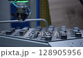 Automated robotic arm handling shiny CNC-machined metal components in a precision-engineering environment. Concept of industrial automation, robotics, and smart manufacturing 128905956