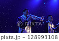 Solo musician in silver costume plays trumpet on blue-lit concert stage 128993108