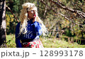 Blonde woman in short skirt gazes thoughtfully into distance in sunny forest clearing 128993178