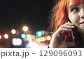 Beautiful red-haired woman smiling, talking on phone at night outdoors against city lights background 129096093