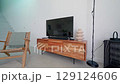 Warm living room highlighting modern entertainment setup with wooden stand, armchair, decorative elements creating inviting, minimalist ambiance for relaxed domestic life 129124606