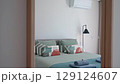 Comfortable bedroom features a large bed with soft pillows and folded towels, a stylish floor lamp, and a discreet air conditioning unit on a clean white wall 129124607