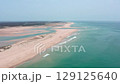 Turquoise waters gently washing sandy shores of faro beach, nestled within ria formosa natural park, featuring tourists leisurely walking along pristine coastline under clear summer skies 129125640