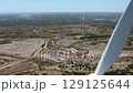 White wind turbine blades rotating, revealing expansive landscape with solar panels, verdant orchards, and serene water body against blue sky and distant horizon 129125644