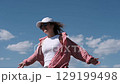 Young joyful woman in white baseball cap and red checkered shirt spinning on the seashore enjoying summer holidays. Vacation, weekend, holidays 129199498