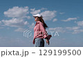 Young joyful woman in white baseball cap and red checkered shirt spinning on the seashore enjoying summer holidays. Vacation, weekend, holidays 129199500