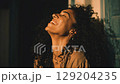 A happy young woman with curly hair smiles with her eyes closed in warm light. 129204235
