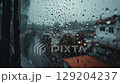 Raindrops cling to a window pane, blurring the city scene outside. 129204237
