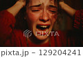 Young woman intensely crying with hands on her head, expressing sorrow and despair. 129204241