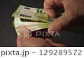 Hands holding and fanning out 100 Euro bills against a dark backdrop 129289572