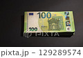 A hand places a stack of 100 Euro banknotes on a dark surface 129289574