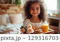 Cute girl with curly hair serves breakfast in a cozy bedroom with flowers and juice 129316703