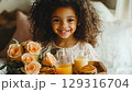 Cute girl with curly hair serves breakfast in a cozy bedroom with flowers and juice 129316704