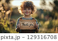 Child holding a wooden sign expressing gratitude during golden hour in a field 129316708