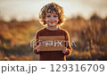 Child holding a wooden sign expressing gratitude during golden hour in a field 129316709