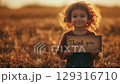 Child expresses gratitude in a sunset-lit wheat field holding a thank you sign 129316710