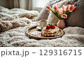 Cozy breakfast in bed with pancakes, strawberries, coffee, and tulips on a soft blanket 129316715