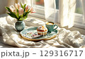Warm morning light highlights a cozy breakfast with flowers, coffee, and a muffin on a soft bedspread 129316717