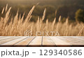 Creative outdoor concept. Empty wooden bridge table in focus with blur defocused dry grass wild meadow blowing in wind at sunset landscape. Template presentation wallpaper banner clip mov 4K HD motion 129340586