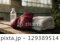 Boxing gloves resting on bench beside water bottle and towel. 129389514