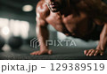 Athlete doing push-ups on gym floor, sweat on mat with dumbbells nearby. 129389519