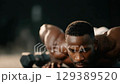 Athlete doing push-ups on gym floor, sweat on mat with dumbbells nearby. 129389520