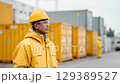 Worker wearing yellow hard hat standing in front of stacked shipping containers. 129389527