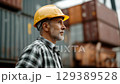 Worker wearing yellow hard hat standing in front of stacked shipping containers. 129389528