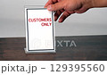 A hand is placing a sign for customers only on a wooden table. 129395560
