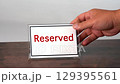 A hand is placing a sign for reserved on a wooden table. 129395561