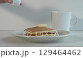 シンプル背景のホットケーキに白いピッチャーからシロップをかける	 129464462