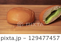 Dolly shot of Three stages of pandanus custard bread on a wooden plate, one whole, one cut in half, and one partially eaten, showing its soft texture and sweet filling 129477457