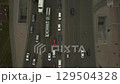 Low-angle drone flight over a massive intersection during early evening rush hour with cyclists riding along the bike path.  129504328