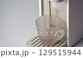The coffee maker is brewing a cup of fresh espresso, with a rich aroma and steam rising from the smooth, dark coffee as it flows into the cup, with a beautiful crema. 129515944