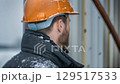 Focused construction worker wearing an orange hard hat in a snowy environment near heavy machinery 129517533