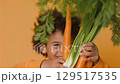 Boy joyfully holding fresh vegetables on his head promoting healthy eating for kids while wearing a bright orange sweatshirt against a yellow backdrop 129517535