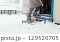 female legs in winter boots and a long down jacket climbs an iron ladder into a garage during a snowfall, side view 129520705