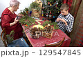 Grandmother and grandson make Christmas wreath together. Elderly woman and teenage boy decorate. Spruces branches and cones 129547845