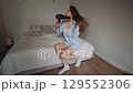 Caucasian girl dries her hair with an electric hairdryer while sitting on the bed at home Lifestyle 129552306