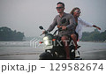 Travelers ride motorbike along sandy sea beach at dusk. Man, woman drive motorcycle on tropical island coastline. Girlfriend embrace her boyfriend, spreads arms, laughs celebrate freedom riding a bike 129582674