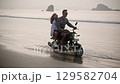 Romantic couple ride motorbike on ocean beach splashing water on date at sunset in slomo. Lovers travel by motorcycle on coastline with reflection, splashes. Girlfriend hugs boyfriend, spreads arms. 129582704