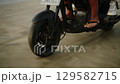 Happy people ride motorbike on seaside. Couple in love have fun driving motorcycle on ocean coast. Girl in sunglasses, bikini embraces boyfriend on romantic scooter trip. Camera tilt from sand, wheel. 129582715
